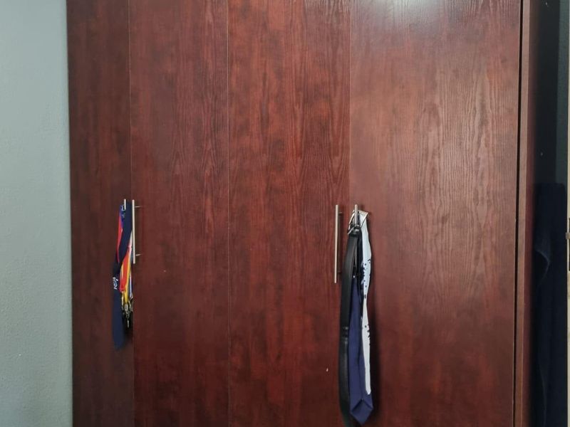 A bedroom featuring a large, dark wood-finish built-in wardrobe with modern metal handles.