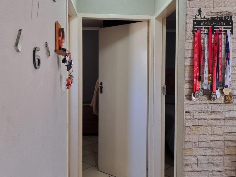 A functional hallway featuring tiled flooring, a textured ceiling, and a stone veneer accent wall leading to adjacent rooms.
