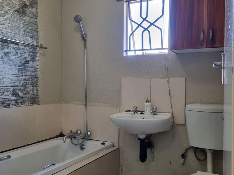 A functional bathroom featuring a bathtub, wall-mounted basin, and toilet, requiring cosmetic updates and repairs to wall finishes and fixtures.