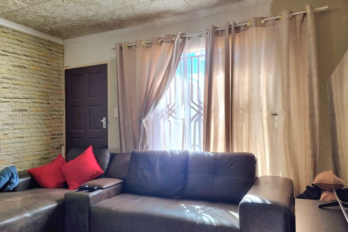 Living room featuring a stone veneer accent wall, textured ceiling tiles, and a window with an integrated security gate.