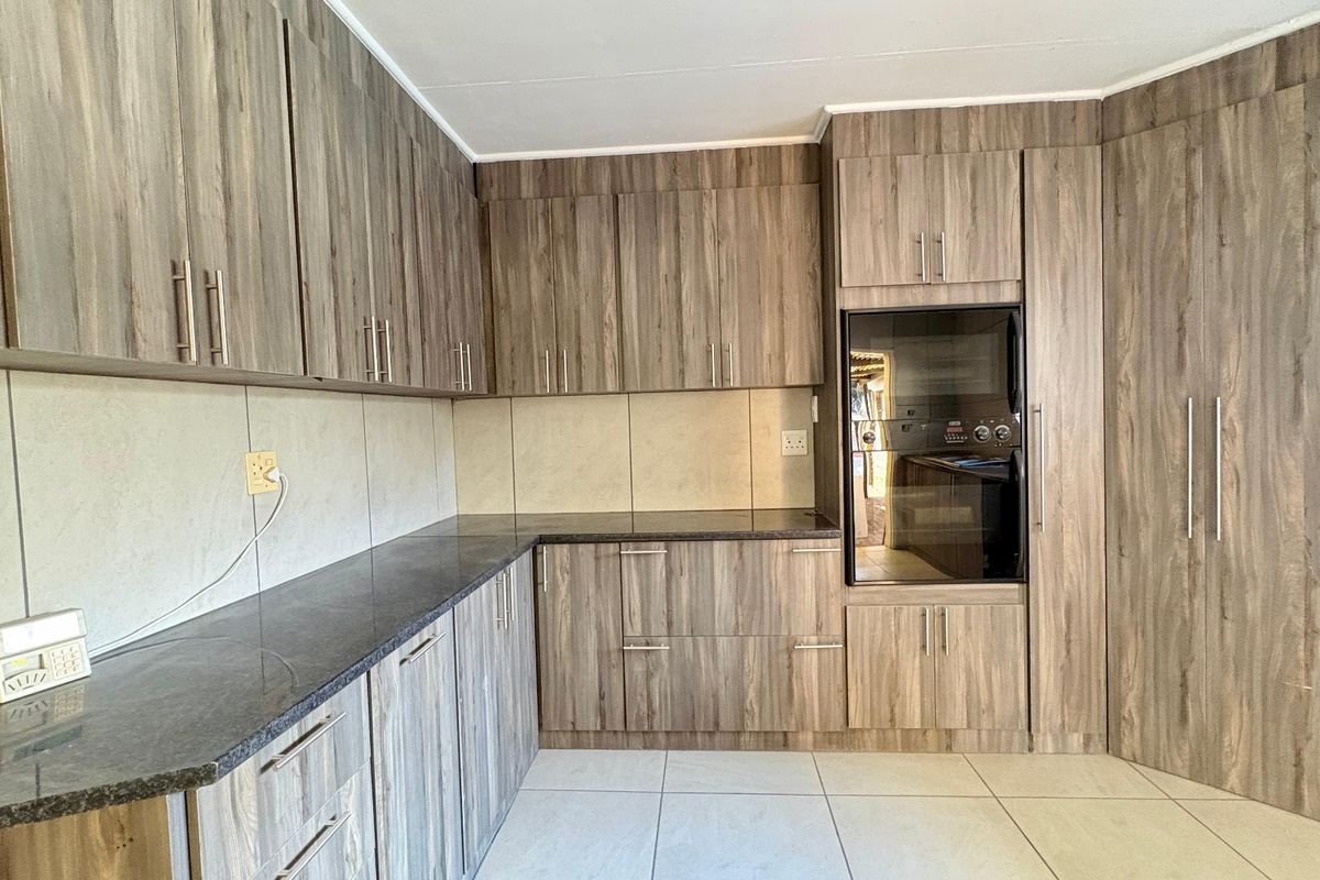 A clean, functional kitchen featuring wood-grain cabinetry, dark laminate countertops, built-in oven, and neutral tiled flooring.