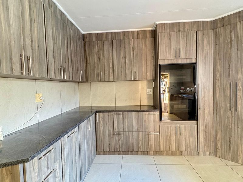 A clean, functional kitchen featuring wood-grain cabinetry, dark laminate countertops, built-in oven, and neutral tiled flooring.