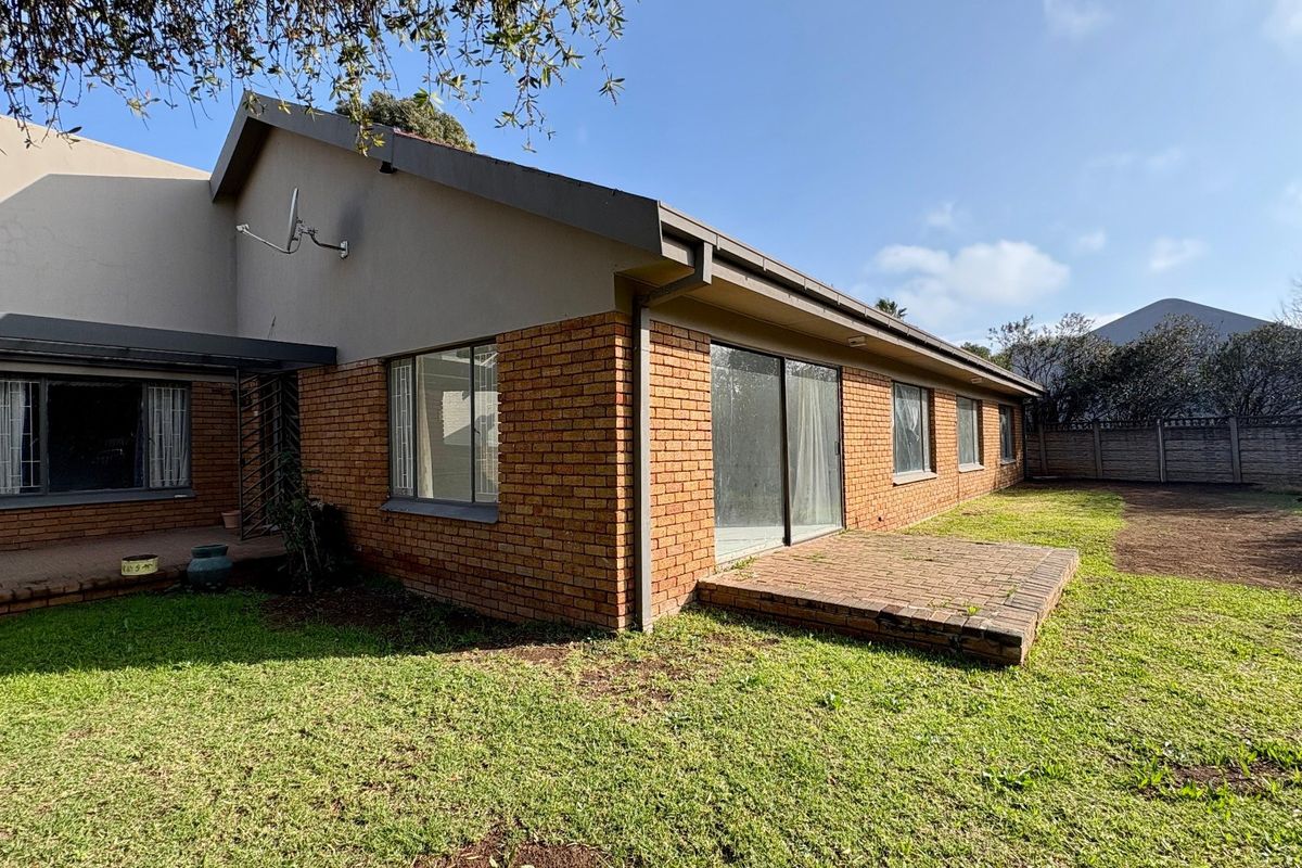 Rear view of the house featuring a brick facade, sliding glass doors leading to a small brick patio, and a spacious backyard.