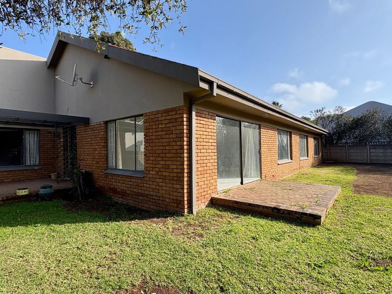 Rear view of the house featuring a brick facade, sliding glass doors leading to a small brick patio, and a spacious backyard.