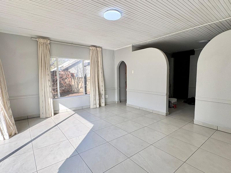 A bright, empty living area featuring neutral tiled flooring, arched architectural wall details, and a clean tongue and groove ceiling finish.