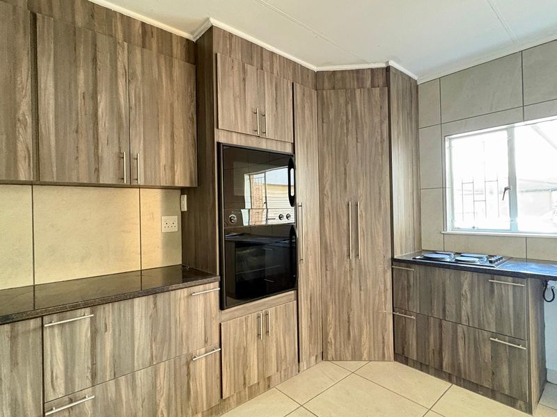 Modern kitchen featuring wood-look cabinetry, built-in oven, hob, dark countertops, and neutral tiled flooring with ample storage space.