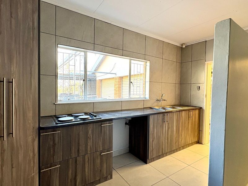 A functional kitchen featuring modern wood-look cabinetry, dark countertops, a built-in electric hob, and a double sink with tiled backsplash.