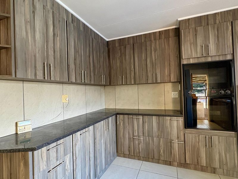 A modern kitchen featuring wood-grain cabinetry, dark granite countertops, a built-in oven, and neutral tiled flooring.