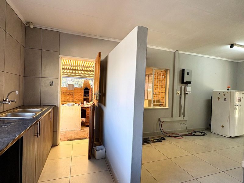 A functional scullery area featuring double sink, tiled splashbacks, built-in cabinetry, and an installed inverter system, with direct access to an outdoor patio.