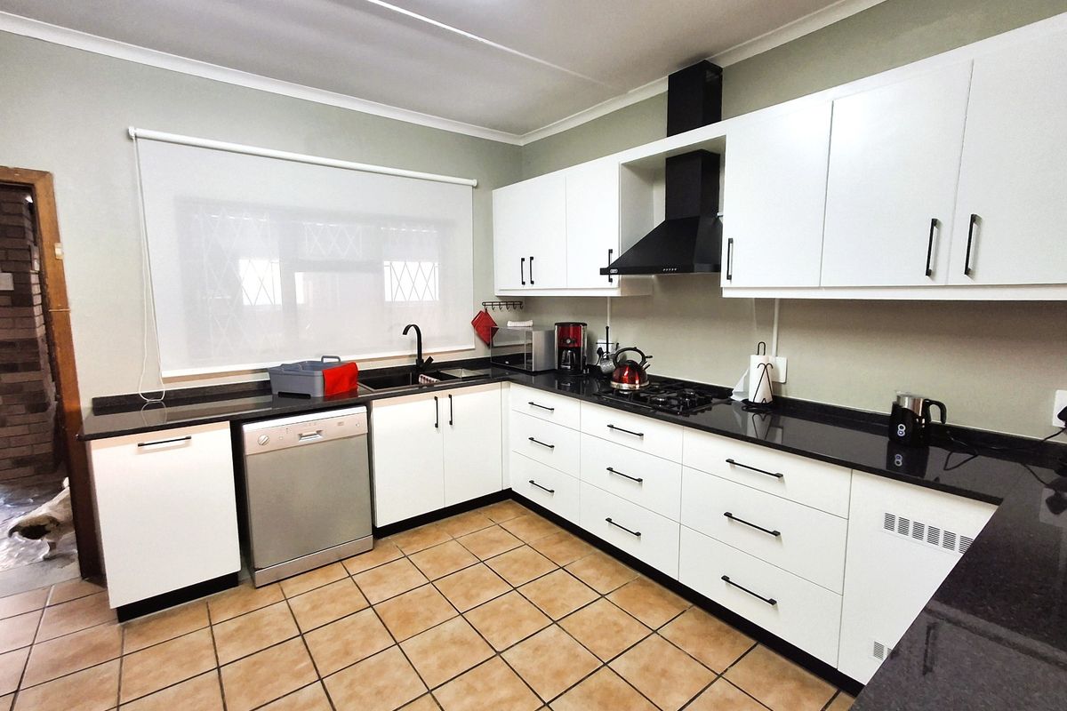 Modern kitchen featuring white cabinetry, contrasting black granite countertops, a gas hob with extractor fan, and tiled flooring.