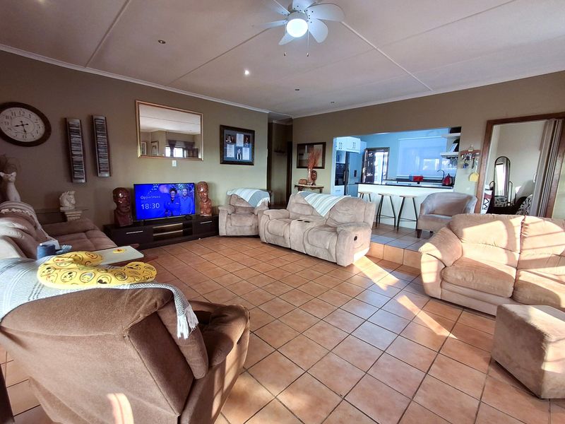 Spacious open-plan living area featuring tiled flooring, a ceiling fan, and a breakfast bar connecting to the kitchen.