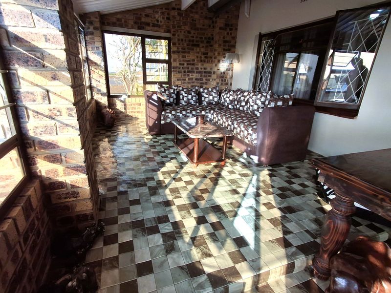 A covered patio area featuring exposed brick walls, large windows, and patterned tiled flooring, providing a bright and functional outdoor living space.
