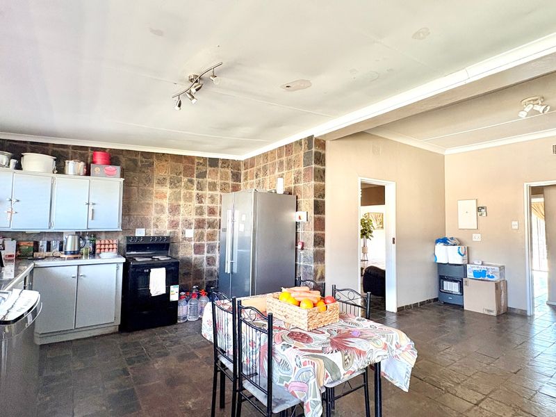 Open-plan kitchen and dining area featuring stone tile flooring, stone backsplash, and built-in cabinetry, requiring some ceiling maintenance.