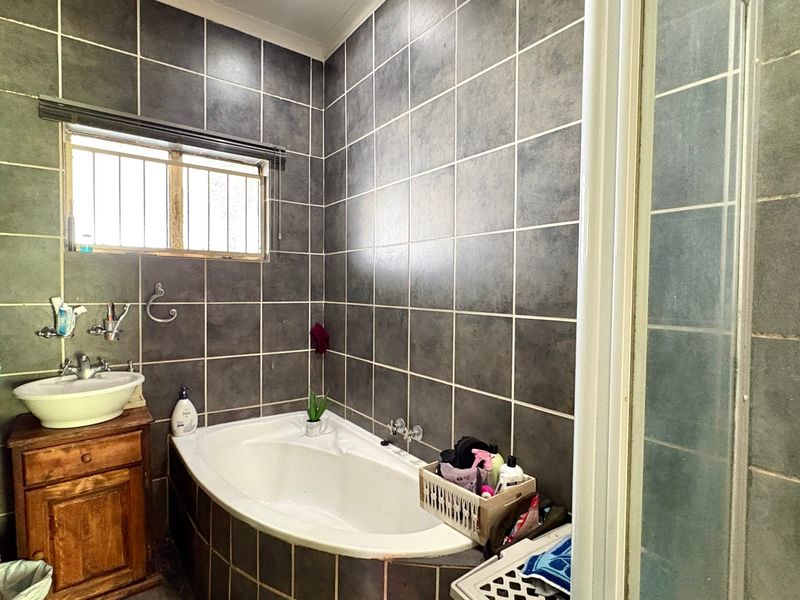 A bathroom featuring dark tiled walls, a built-in corner bathtub, a vessel sink with a wooden vanity, and a separate shower enclosure.