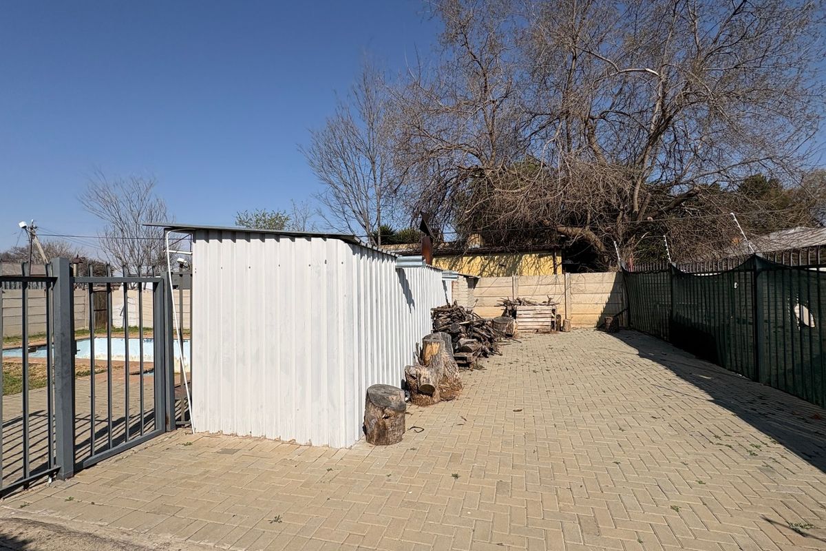 Rear exterior area featuring paved ground, metal fencing, a corrugated metal storage shed, and a swimming pool.