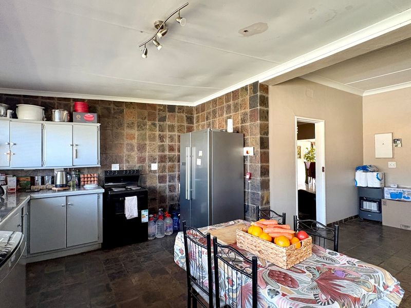 Open-plan kitchen and dining area featuring stone-clad walls, tiled flooring, and built-in cabinetry, offering a functional space with potential for modern updates.