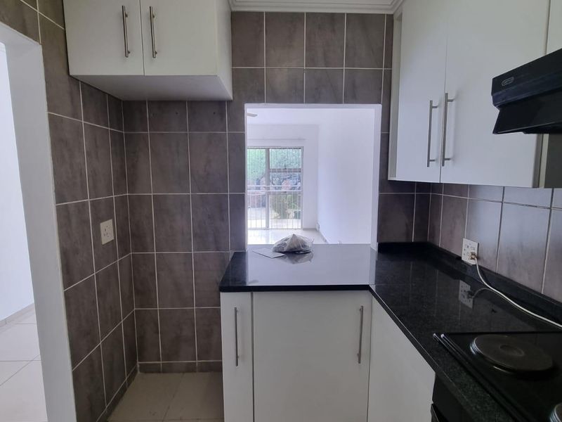 A clean, functional kitchen featuring white cabinetry, dark granite countertops, built-in oven and hob, and neutral tiled finishes throughout.