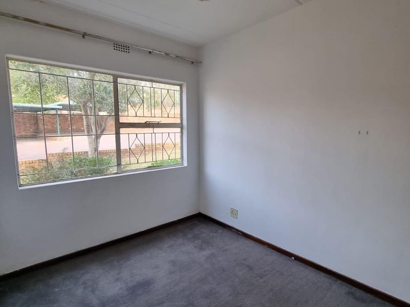 An empty bedroom featuring a ceiling fan, security bars on the window, and carpet flooring, ready for a fresh update.