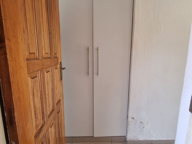 A bedroom featuring a built-in wardrobe with white doors and tiled flooring, showing signs of wall surface wear.