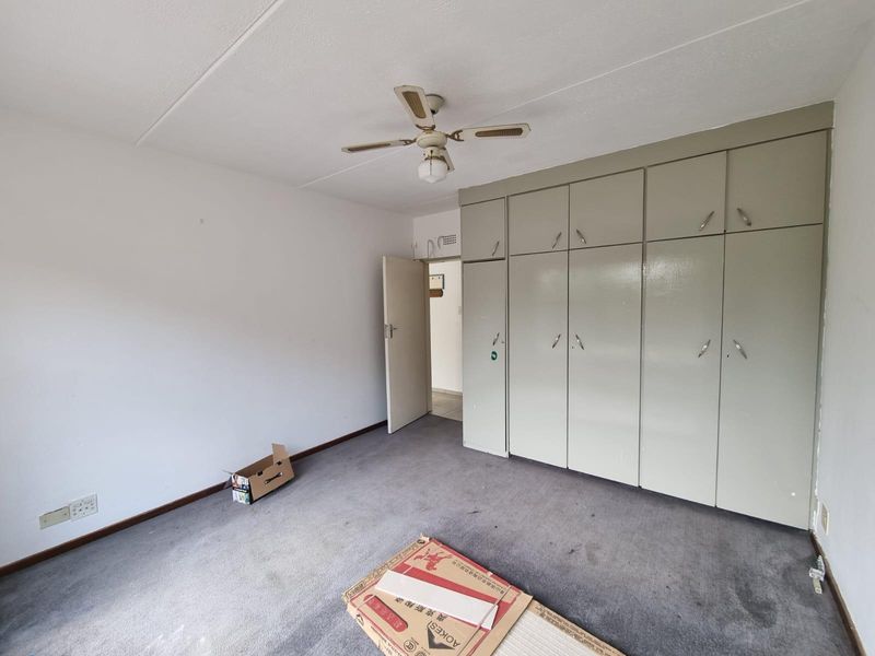 A vacant bedroom featuring built-in cupboards, a ceiling fan, and carpeted flooring, offering a blank canvas for potential updates and personalization.