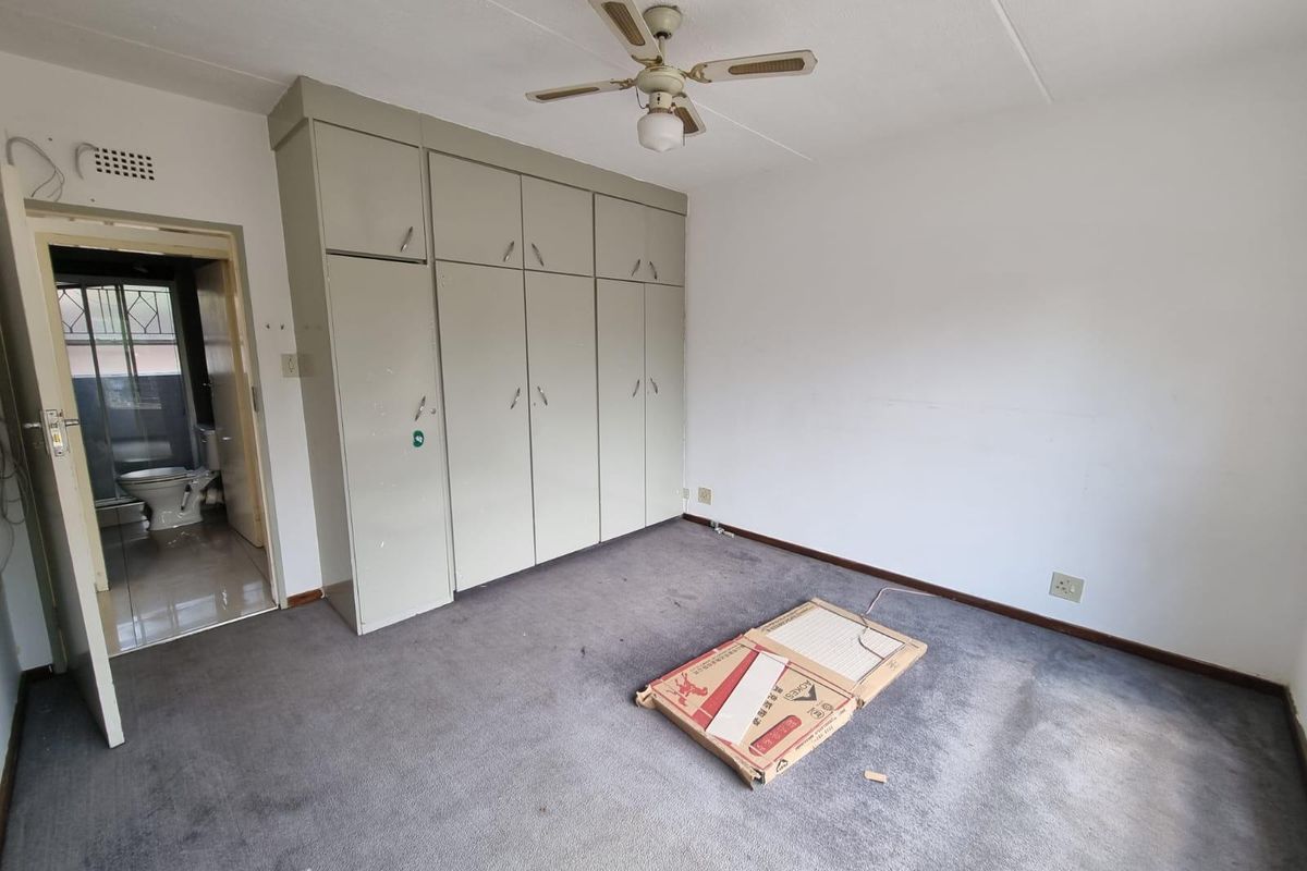 A spacious bedroom featuring built-in cupboards, a ceiling fan, and carpet flooring, with direct access to an en-suite bathroom.
