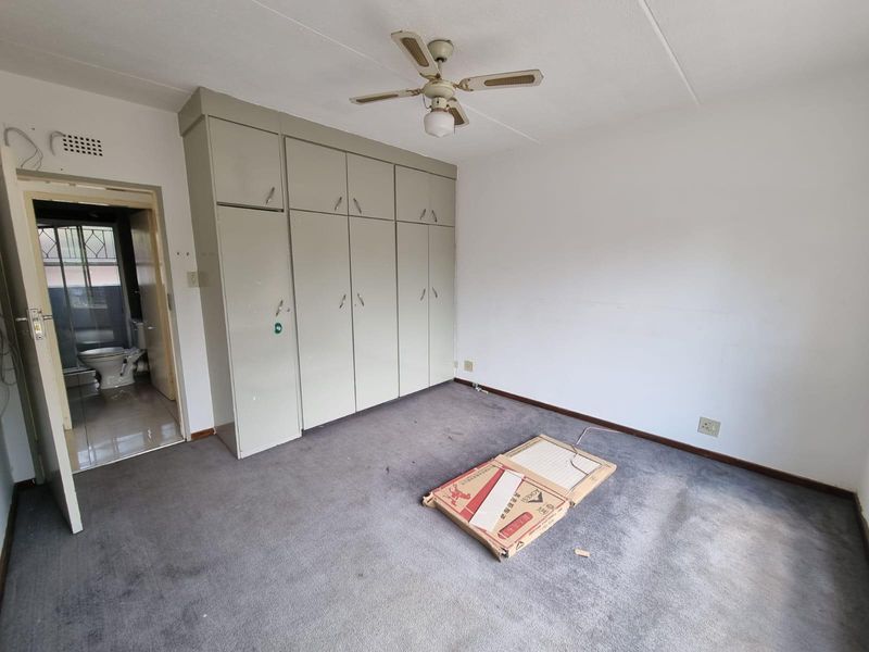 A spacious bedroom featuring built-in cupboards, a ceiling fan, and carpet flooring, with direct access to an en-suite bathroom.
