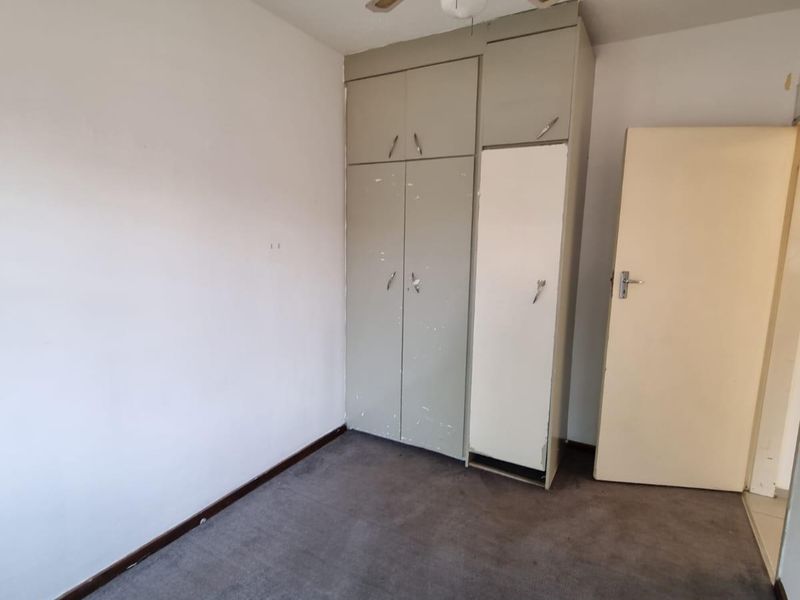 A vacant bedroom featuring built-in cupboards, a ceiling fan, and carpeted flooring, presenting a blank canvas for potential updates.