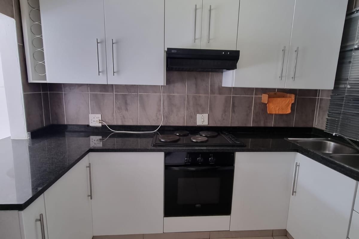 A clean and functional kitchen featuring white cabinetry, dark granite countertops, a built-in oven, electric hob, and neutral tiled flooring.