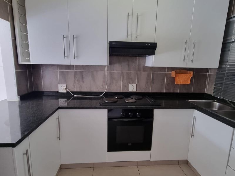 A clean and functional kitchen featuring white cabinetry, dark granite countertops, a built-in oven, electric hob, and neutral tiled flooring.