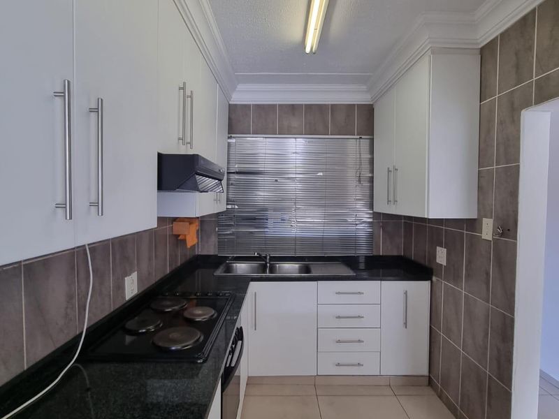 A clean, functional kitchen featuring white cabinetry, dark granite countertops, a built-in electric hob, and neutral tiled finishes.