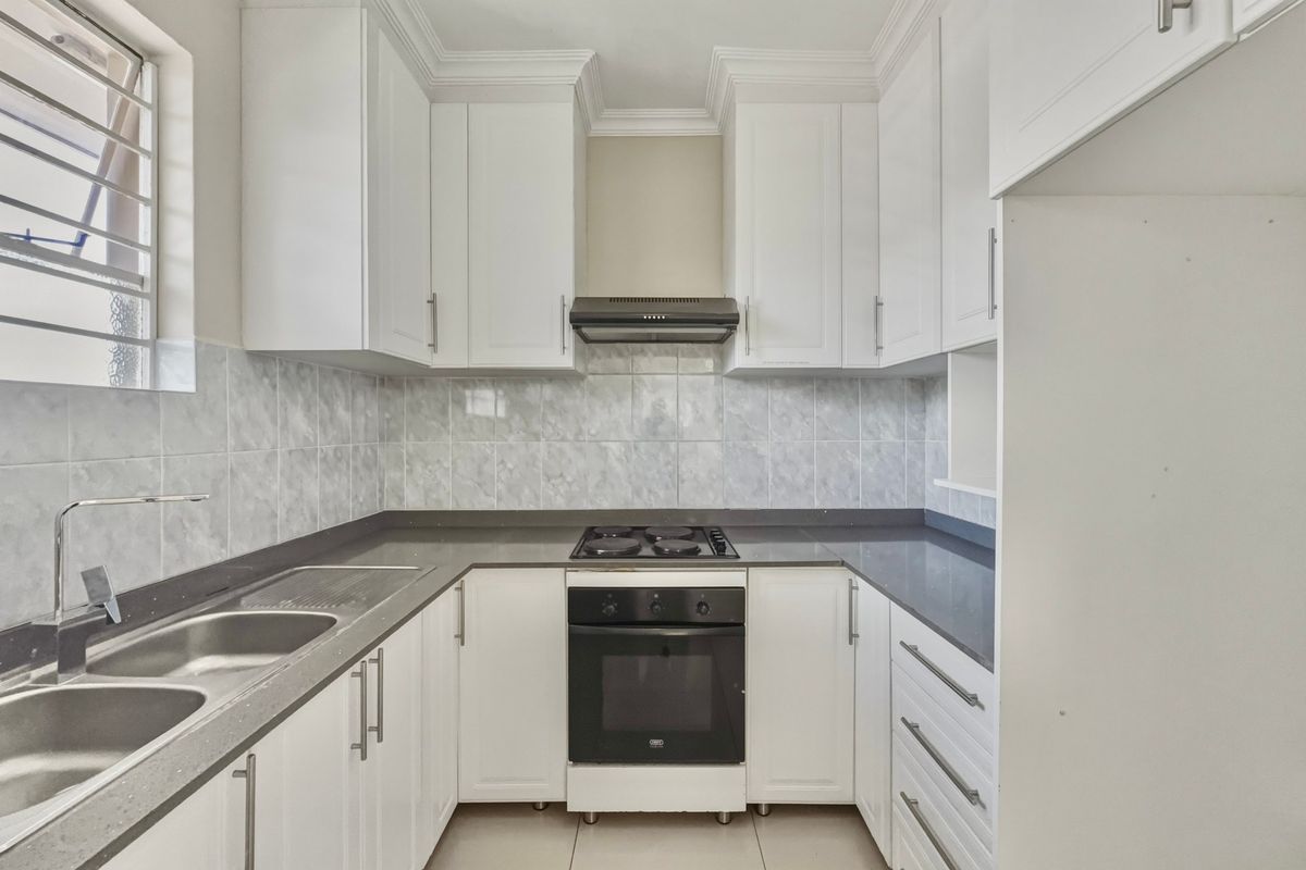 A clean, functional kitchen featuring white cabinetry, dark stone countertops, a built-in oven, electric hob, and a double bowl stainless steel sink.