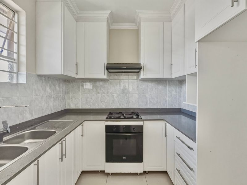 A clean, functional kitchen featuring white cabinetry, dark stone countertops, a built-in oven, electric hob, and a double bowl stainless steel sink.