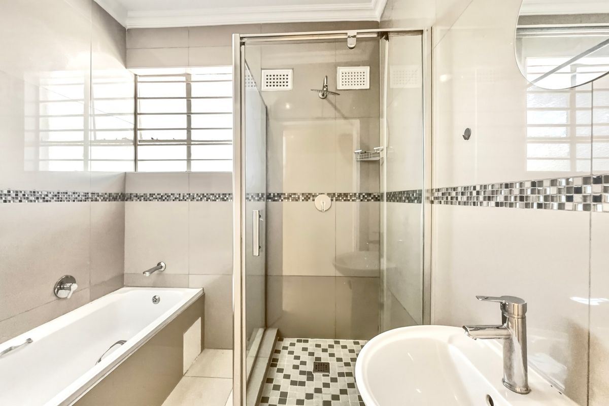 Modern bathroom featuring a separate shower enclosure, bathtub, basin with mixer tap, and neutral tiled walls with a decorative mosaic border.