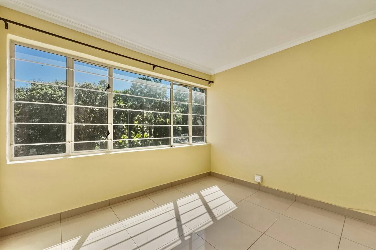 A bright, empty bedroom featuring neutral tiled flooring, large windows with security bars, and clean yellow walls, offering a blank canvas for personalization.