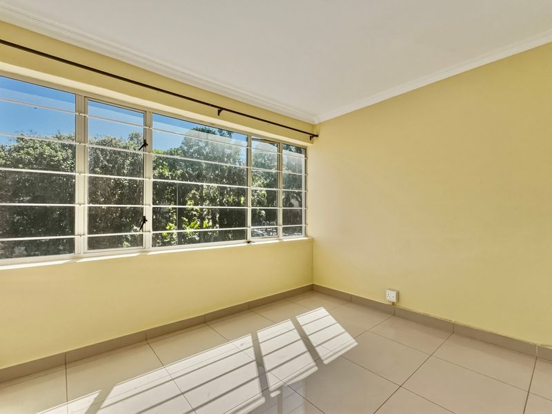 A bright, empty bedroom featuring neutral tiled flooring, large windows with security bars, and clean yellow walls, offering a blank canvas for personalization.