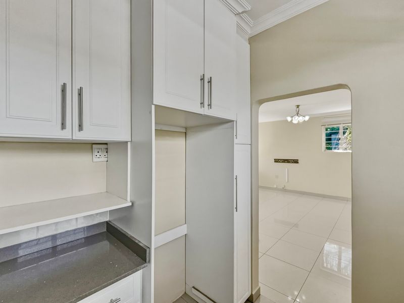 A clean, modern kitchen area featuring white built-in cabinetry, stone countertops, and tiled flooring, with an open archway leading into the adjacent living space.