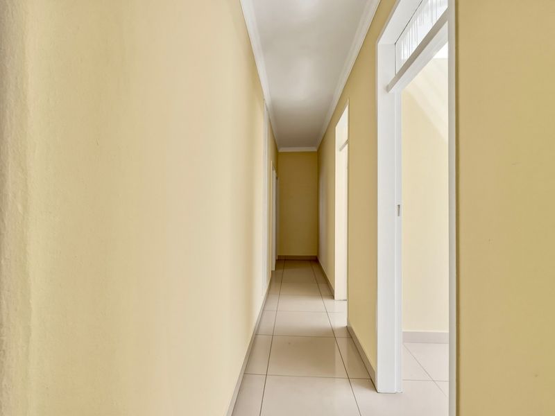 A clean, empty hallway featuring neutral yellow walls and light-colored floor tiles, providing access to multiple rooms within the apartment.