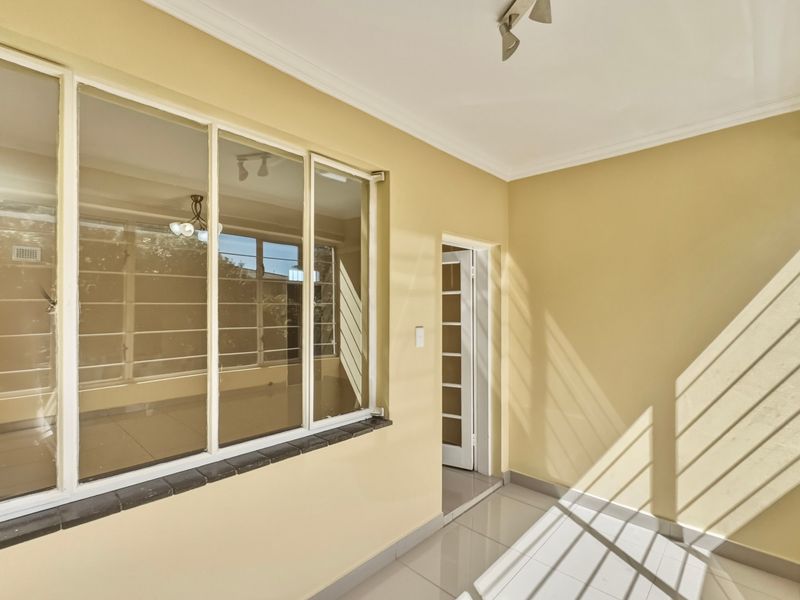 A bright, enclosed balcony or sunroom featuring tiled flooring, large windows, and neutral wall finishes, offering a versatile space for relaxation.