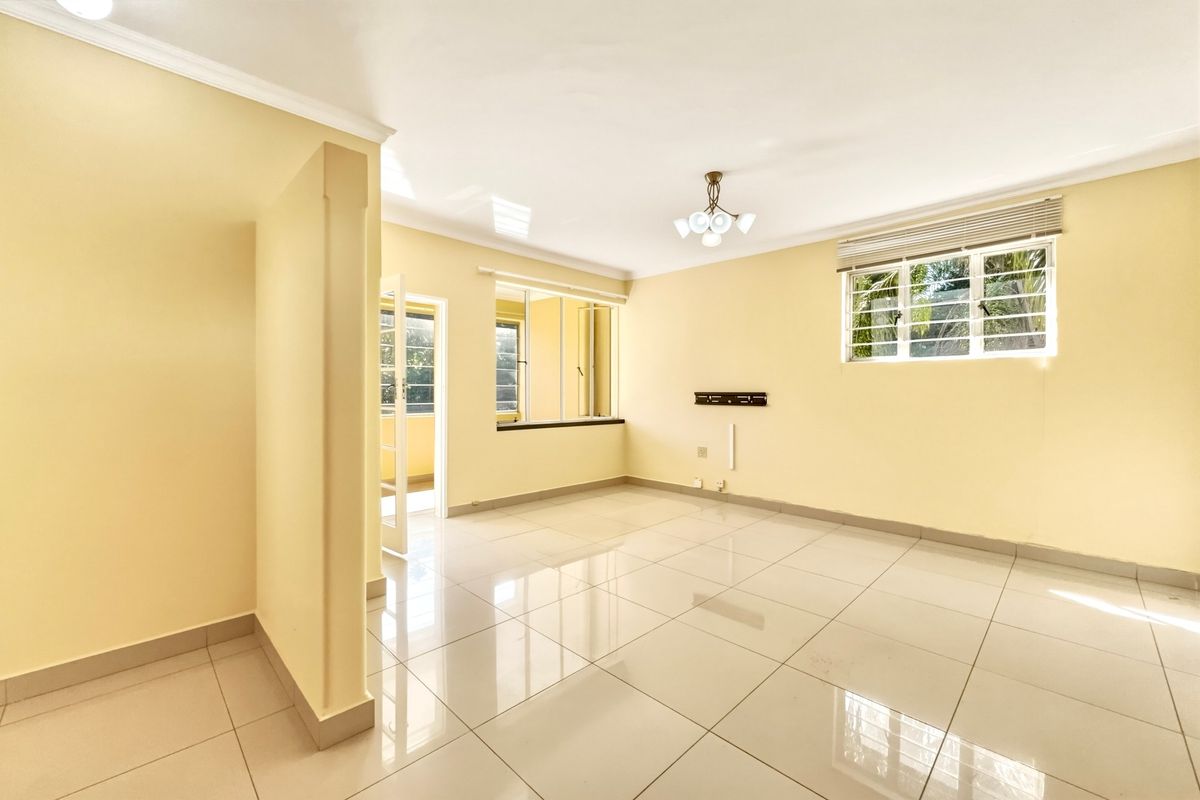 A bright, empty living room featuring neutral tiled flooring, coved ceilings, and large windows with security bars, offering a clean canvas for personalization.