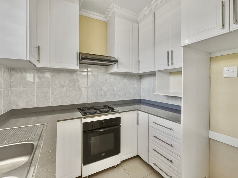 A clean, modern kitchen featuring white cabinetry, grey stone countertops, built-in oven, electric hob, and a tiled backsplash.