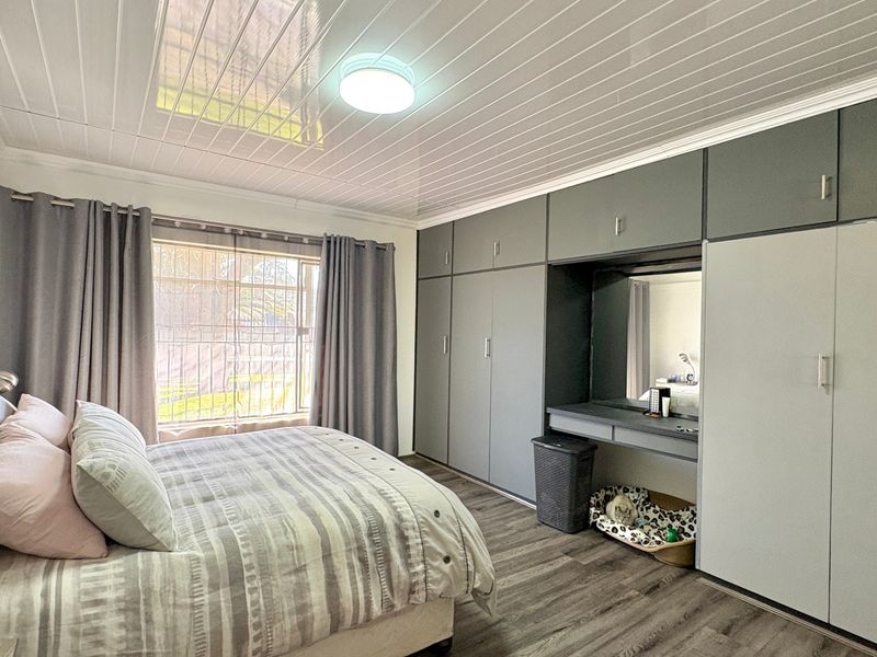 A well-maintained bedroom featuring extensive built-in cupboards with an integrated vanity, laminate flooring, and a modern ceiling finish.