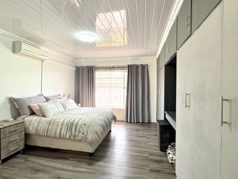 Spacious bedroom featuring built-in cupboards, laminate flooring, a split-system air conditioner, and a modern PVC ceiling finish.