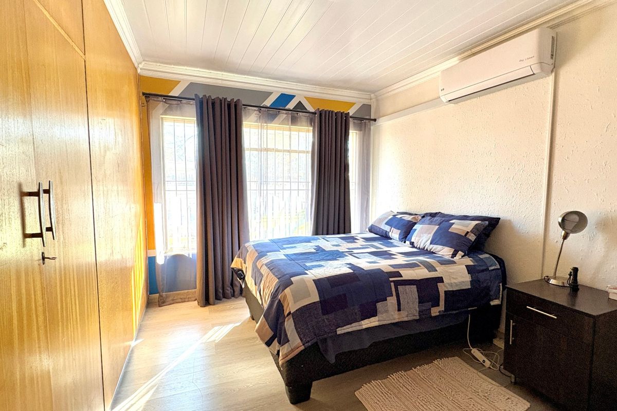 A bedroom featuring built-in wooden cupboards, an air conditioning unit, and security bars on the window, providing a functional and comfortable living space.