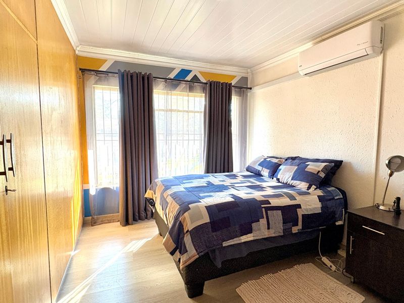 A bedroom featuring built-in wooden cupboards, an air conditioning unit, and security bars on the window, providing a functional and comfortable living space.