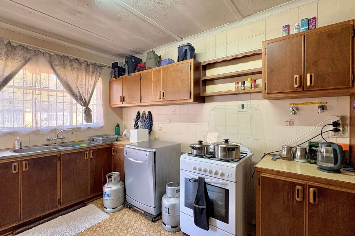 A dated kitchen featuring wooden cabinetry, laminate countertops, a stainless steel double sink, and a freestanding gas stove with tiled backsplash.