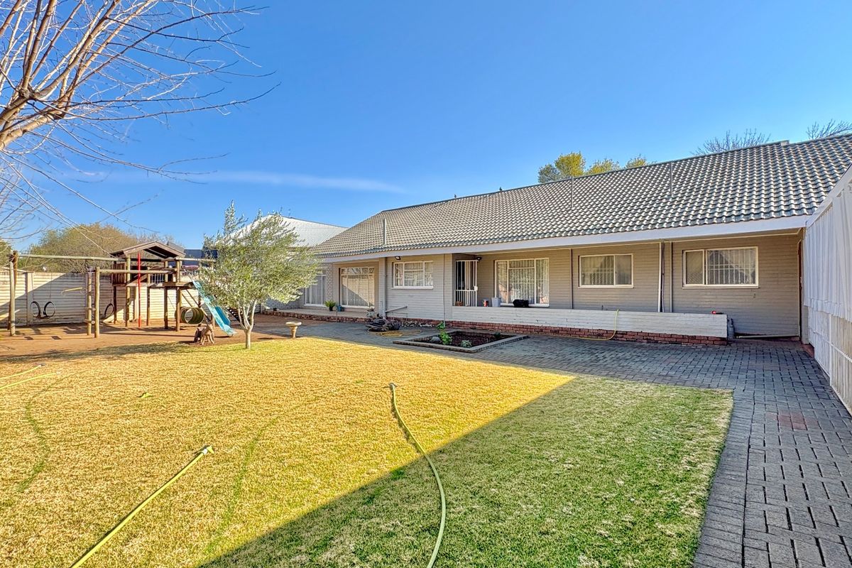 Rear view of the property featuring a paved patio area, established lawn, and a tiled roof structure with security bars on windows.