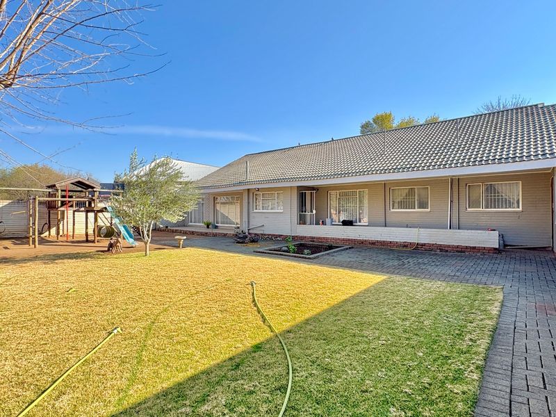 Rear view of the property featuring a paved patio area, established lawn, and a tiled roof structure with security bars on windows.