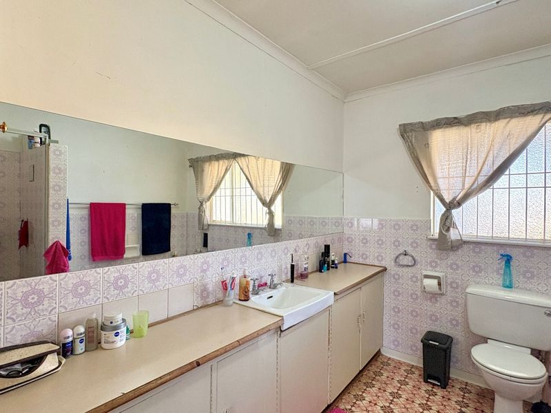 A dated bathroom featuring a long vanity with integrated basin, large wall mirror, patterned wall tiles, and a standard toilet.