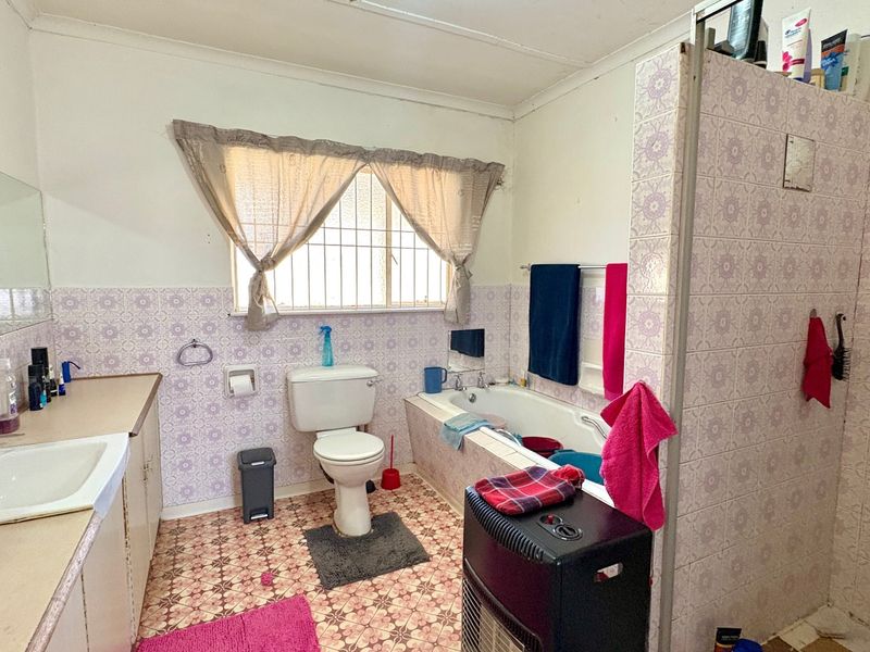 A dated bathroom featuring a built-in vanity, bathtub, and separate shower enclosure with patterned wall tiles and original floor tiling.