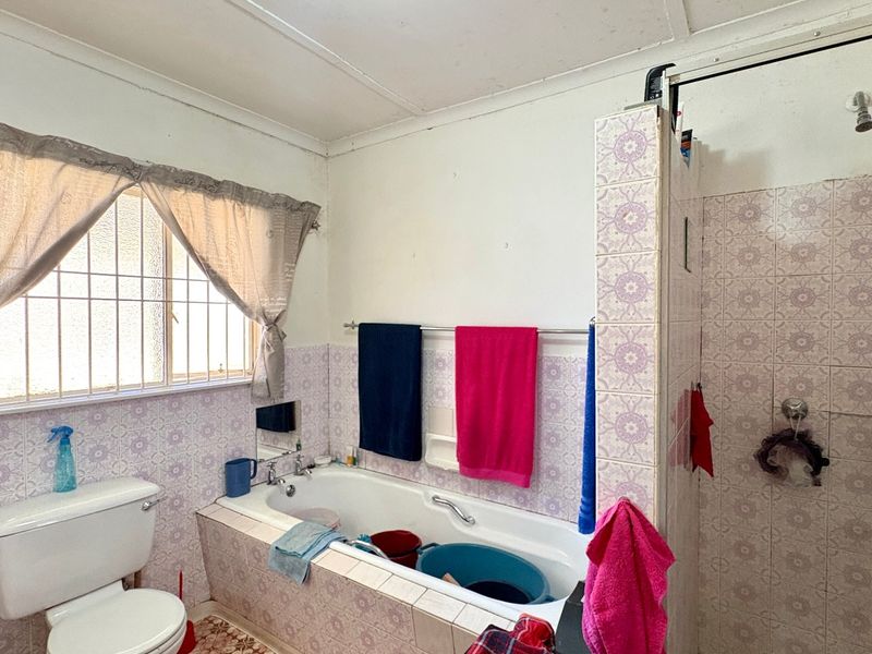 A dated bathroom featuring a built-in bathtub, separate shower enclosure, and toilet, with original patterned wall tiling throughout.